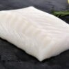 Fresh raw Alaskan cod fillet on dark slate with lemon and rosemary