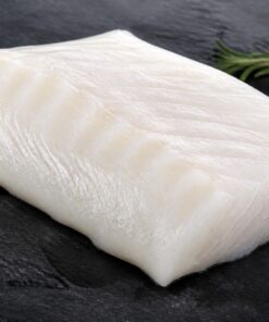 Fresh raw Alaskan cod fillet on dark slate with lemon and rosemary